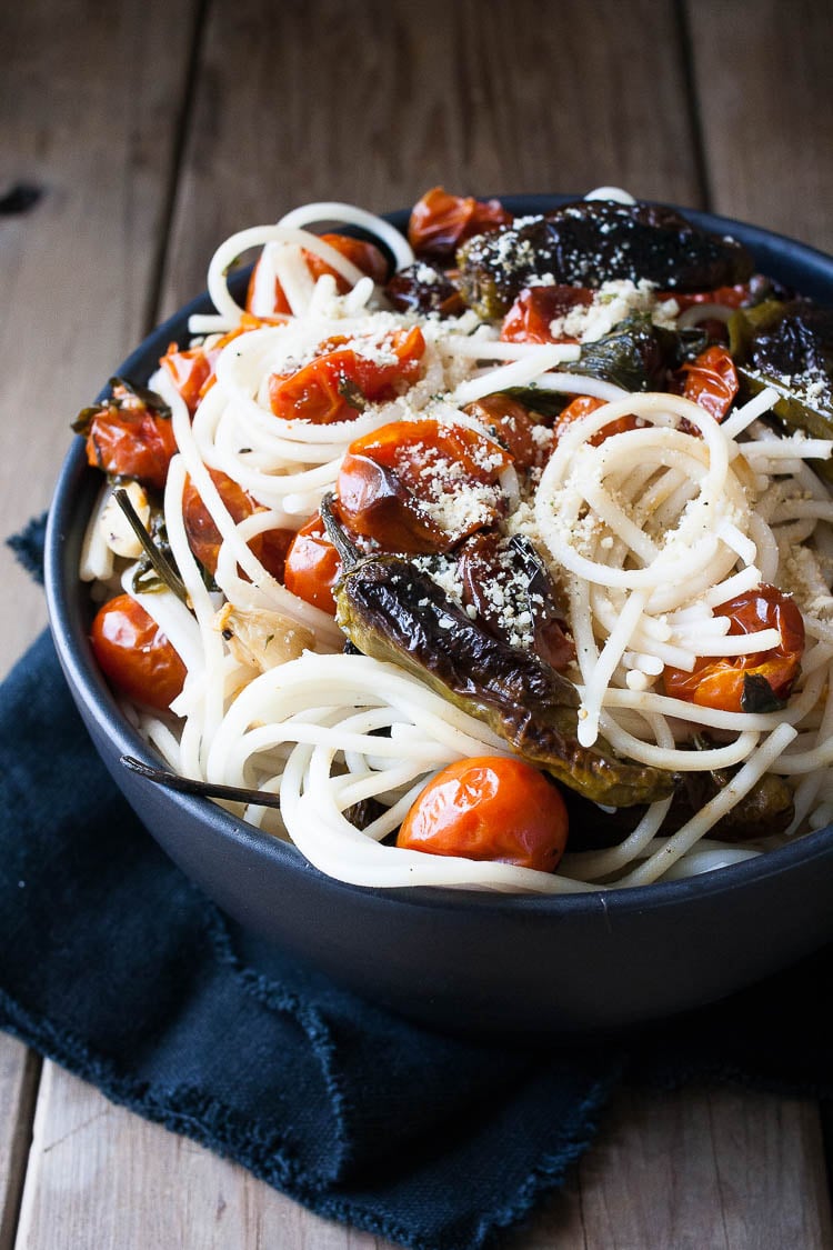 A close up shot of spaghetti in a bowl with charred tomatoes