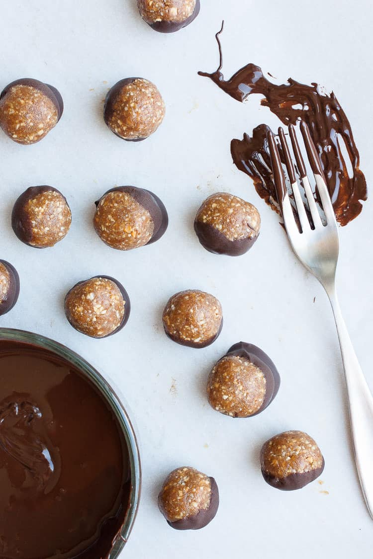 Raw Vegan Caramel Peanut Protein Truffles on a white surface with melted chocolate in a bowl