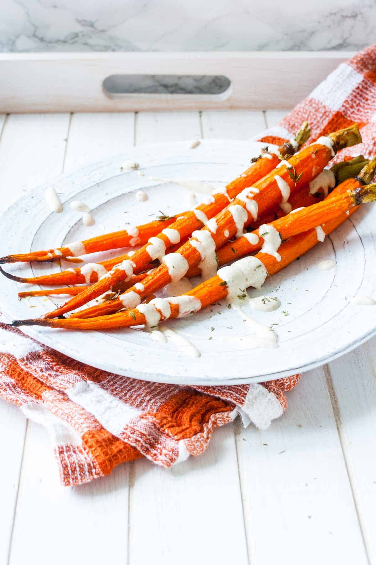 A side shot of a group of roasted carrots with a white drizzle and thyme on a white plate.