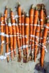 A line of roasted carrots on a piece of parchment paper with a white drizzle over them.