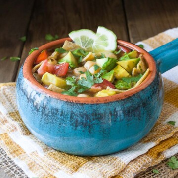 A blue bowl filed with Vegan Chickpea Soup sitting on a wooden surface and topped with lime wedges