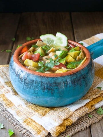 A blue bowl filed with Vegan Chickpea Soup sitting on a wooden surface and topped with lime wedges