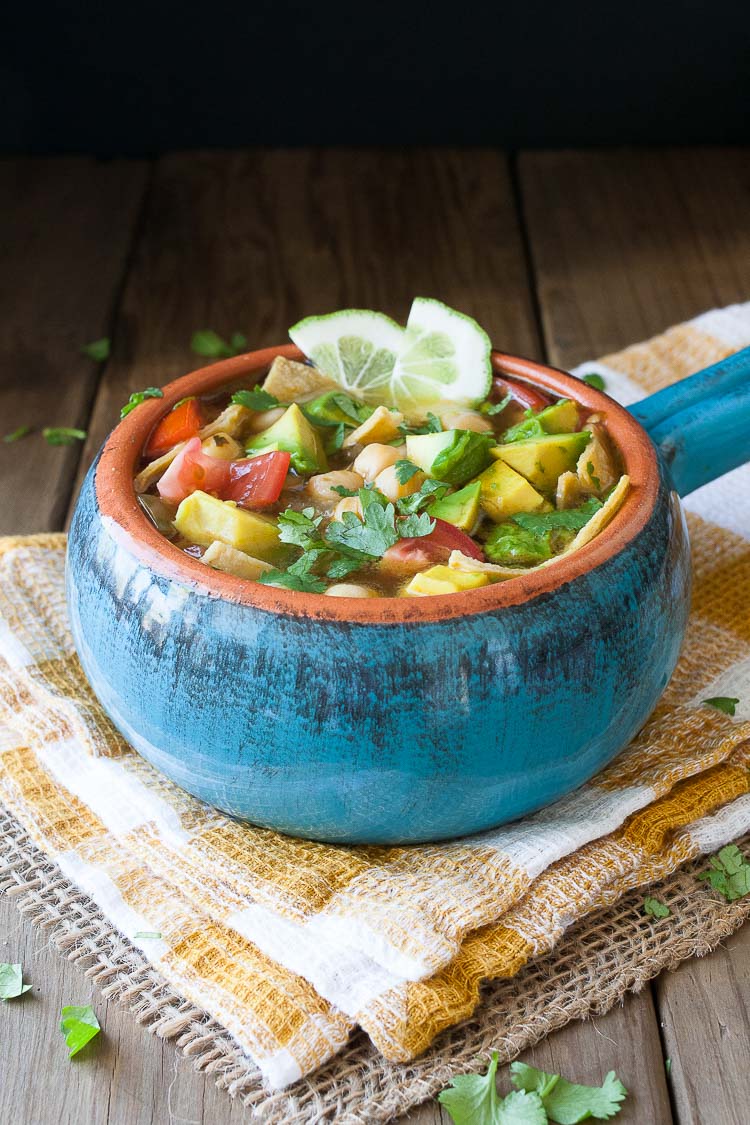 A blue bowl filed with Vegan Chickpea Soup sitting on a wooden surface and topped with lime wedges