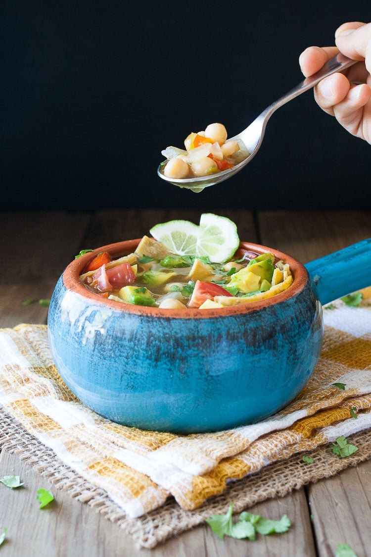 A blue bowl filled with vegan chickpea soup and a spoon taking some out