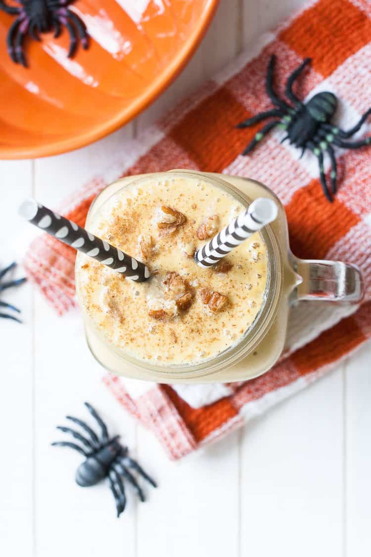 An overhead shot of a light peach colored smoothie topped with pecans in a glass jar