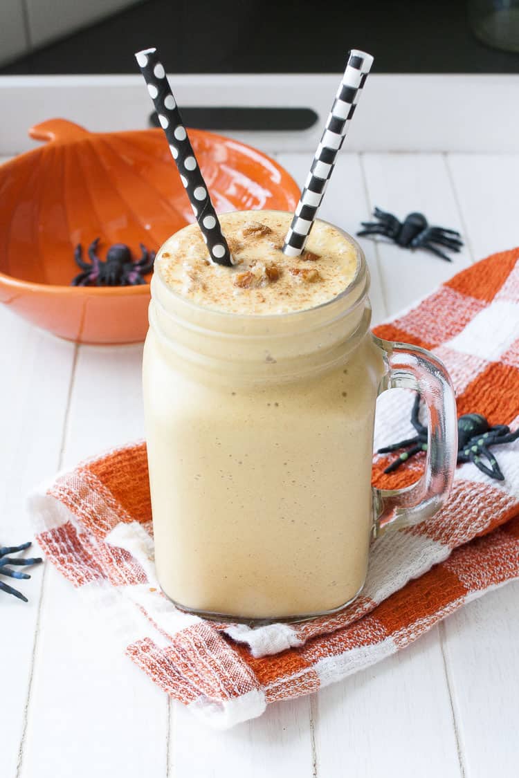 A light peach colored smoothie in a glass jar with black and white straws