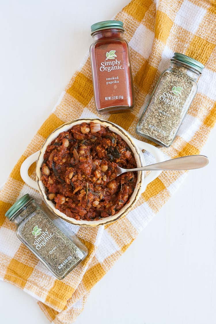 An overhead shot of spiced smoked tomato sauce with chickpeas in a bowl with spice jars all around it