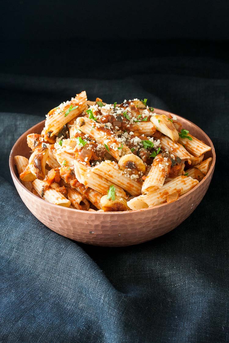 A side shot of Chickpeas in Spicy Smoked Tomato Sauce with Penne in a bowl topped with vegan parmesan cheese