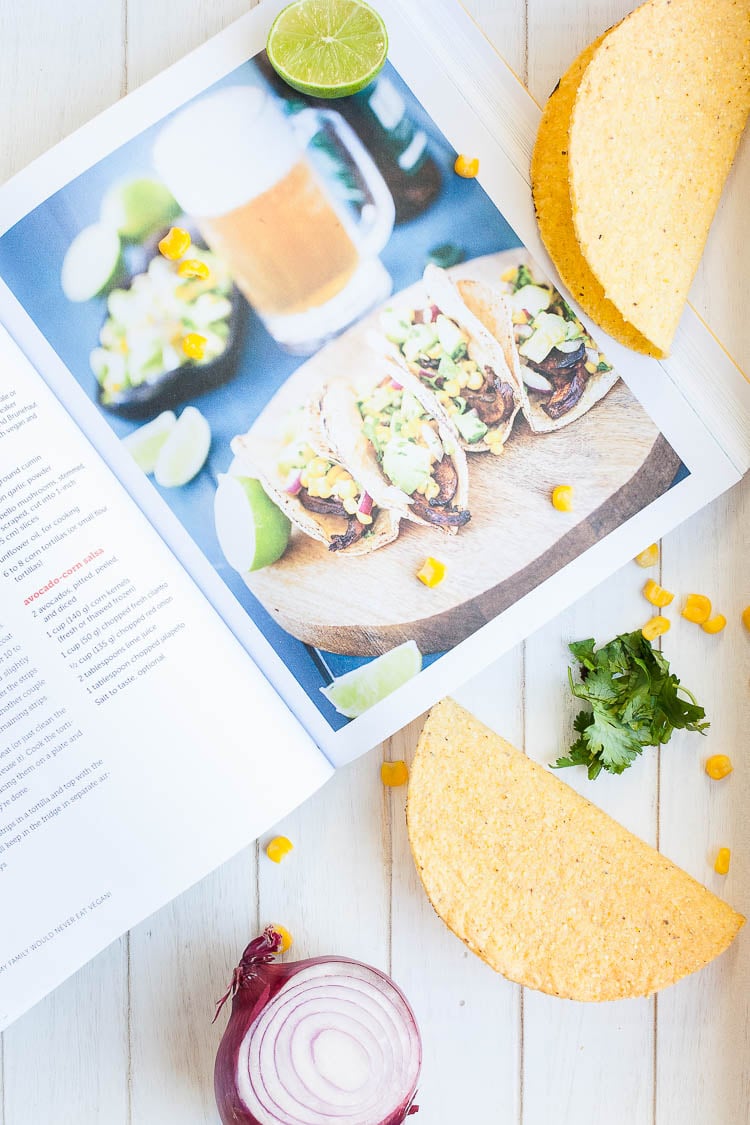 A cookbook open at Beer-Marinated Portobello Mushroom Tacos sitting on a wooden surface