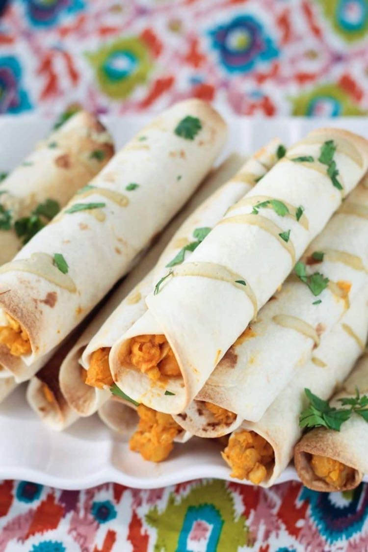 Taquitos with buffalo sauce chickpea filling piled on a white plate