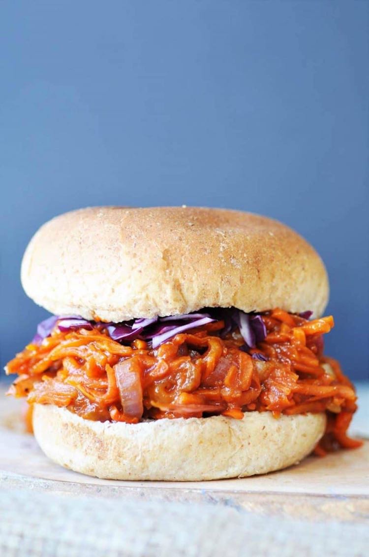 Sandwich filled with shredded carrots smothered in bbq sauce and topped with red cabbage