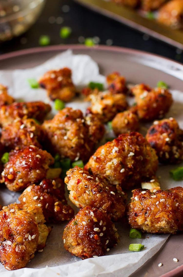 Cauliflower pieces covered in sesame maple sauce sitting on a white towel on a grey plate