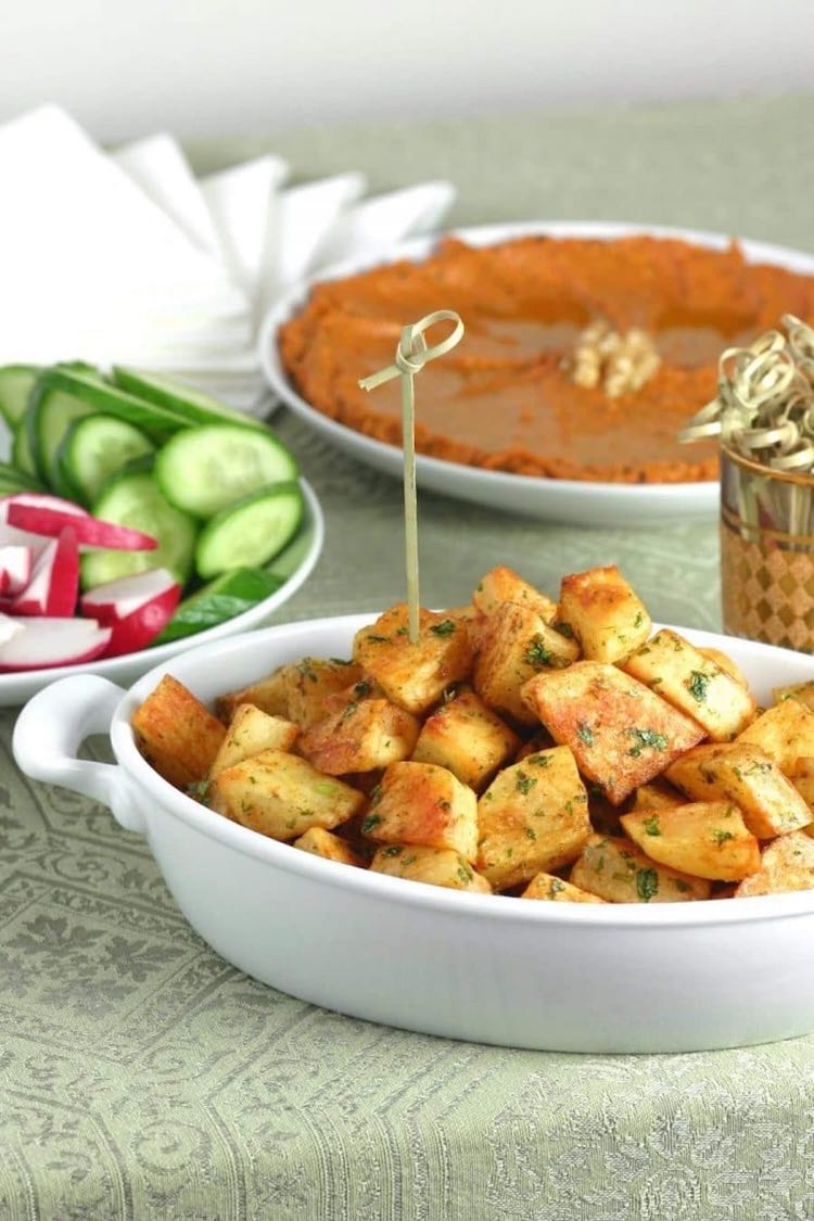 White baking dish filled with cubes potatoes with herbs in front of veggies and dip