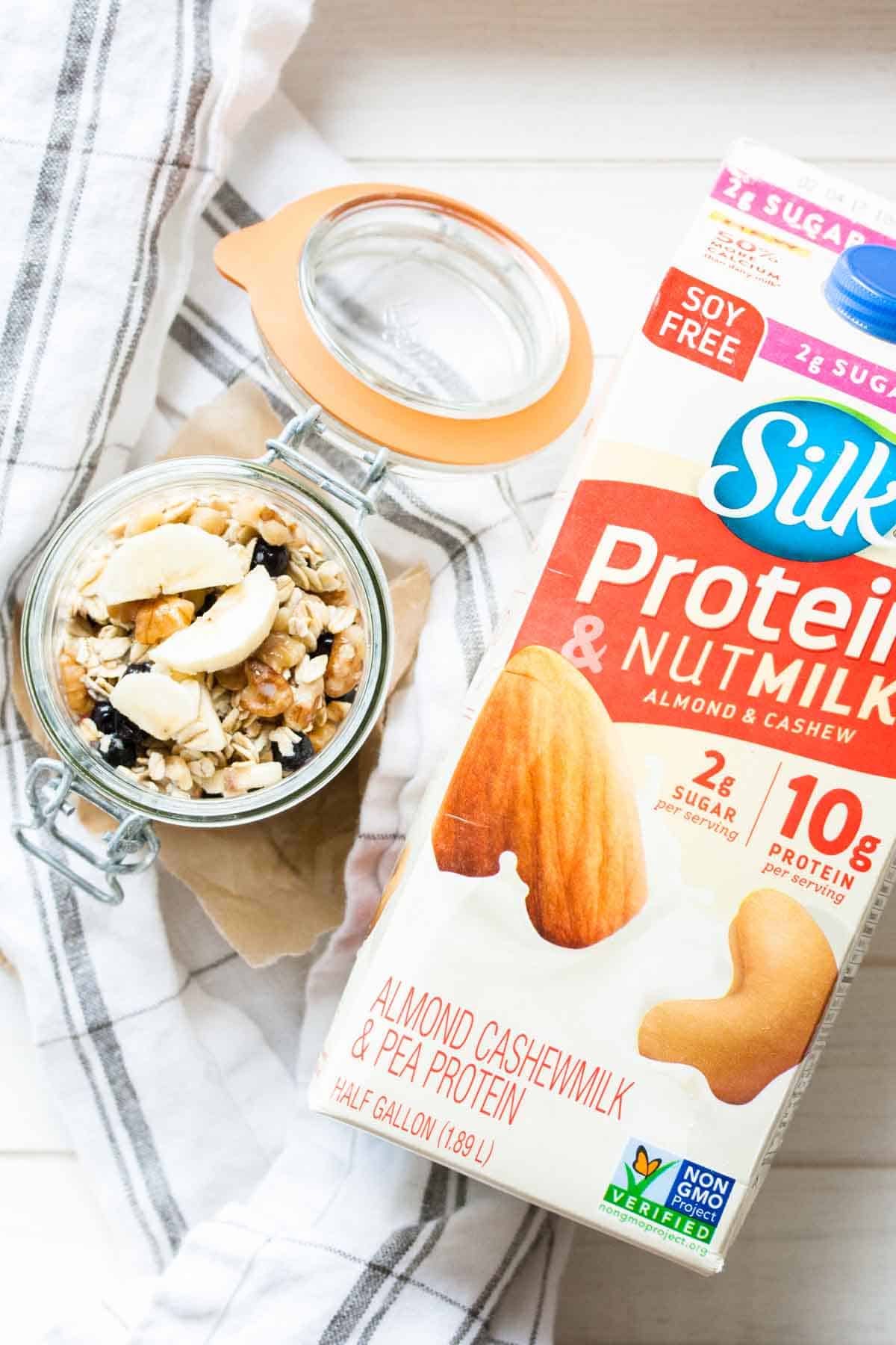 A carton of silk nutmilk laying flat on a wooden surface with a jar of cereal next to it
