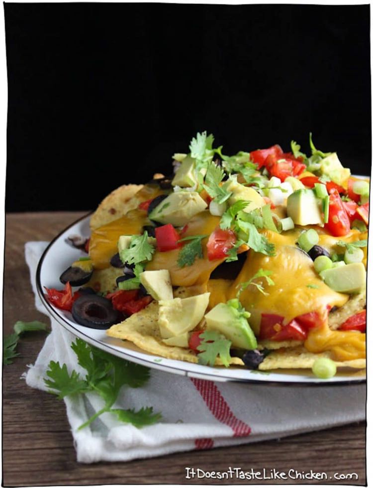 White bowl filled with nachos topped with cilantro, tomatees, avocados and olives