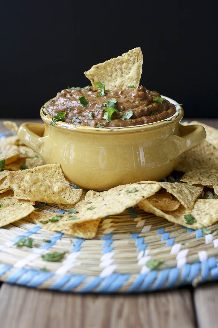 Yellow bowl filled with chili cheese dip and topped with cilantro and a chip