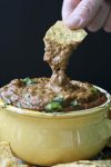 Hand dipping chip into yellow bowl of gooey chili cheese dip