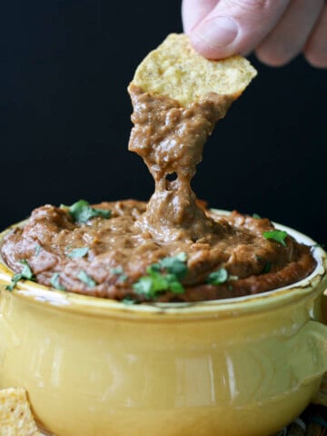 Hand dipping chip into yellow bowl of gooey chili cheese dip