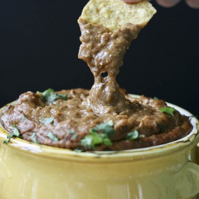 Hand dipping chip into yellow bowl of gooey chili cheese dip