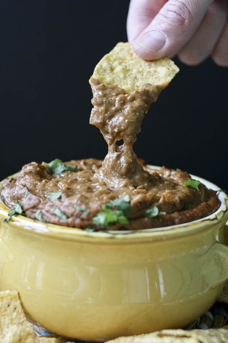 Hand dipping chip into yellow bowl of gooey vegan chili cheese dip