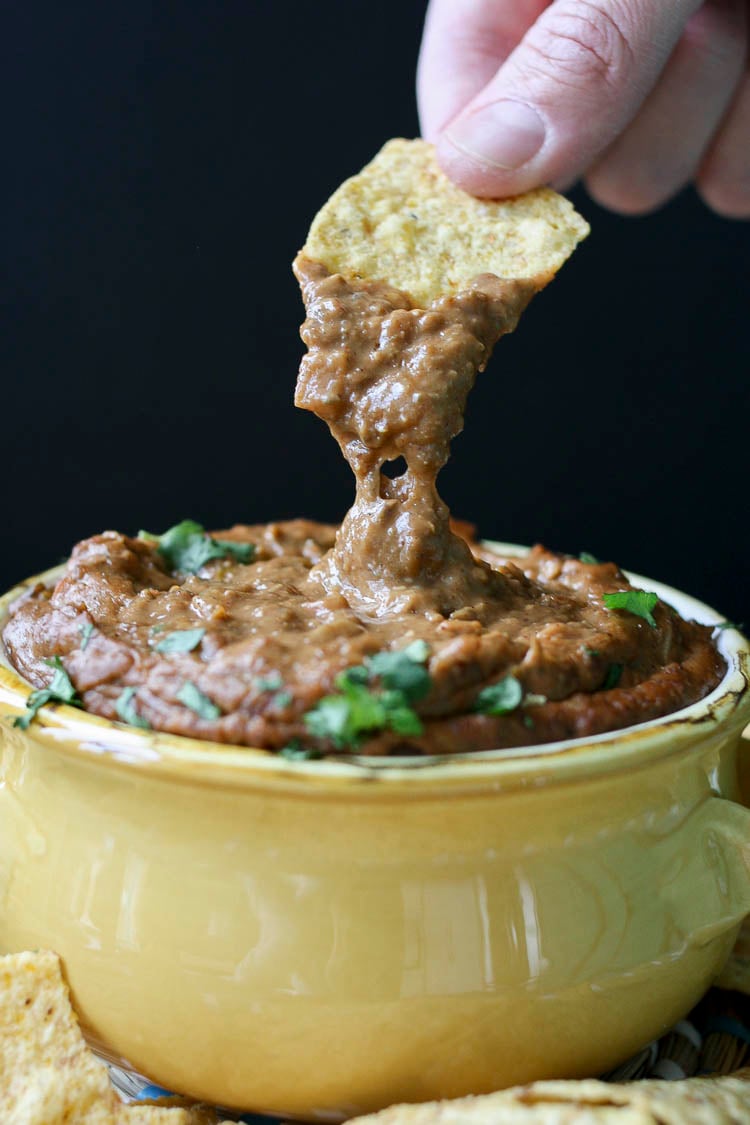 Hand dipping chip into yellow bowl of gooey vegan chili cheese dip