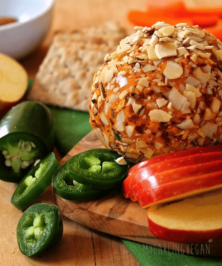 Cheese ball rolled in sliced almonds on a board with sliced apples and jalapeños