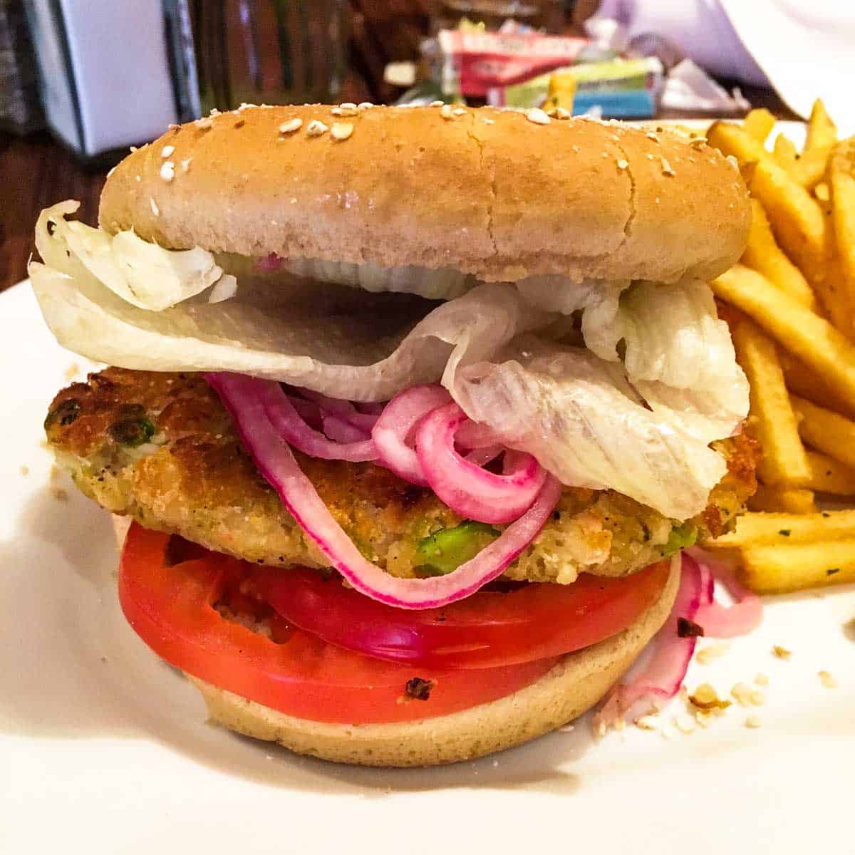 Front view of a veggie burger topped with tomatoes, red onions and lettuce with fries