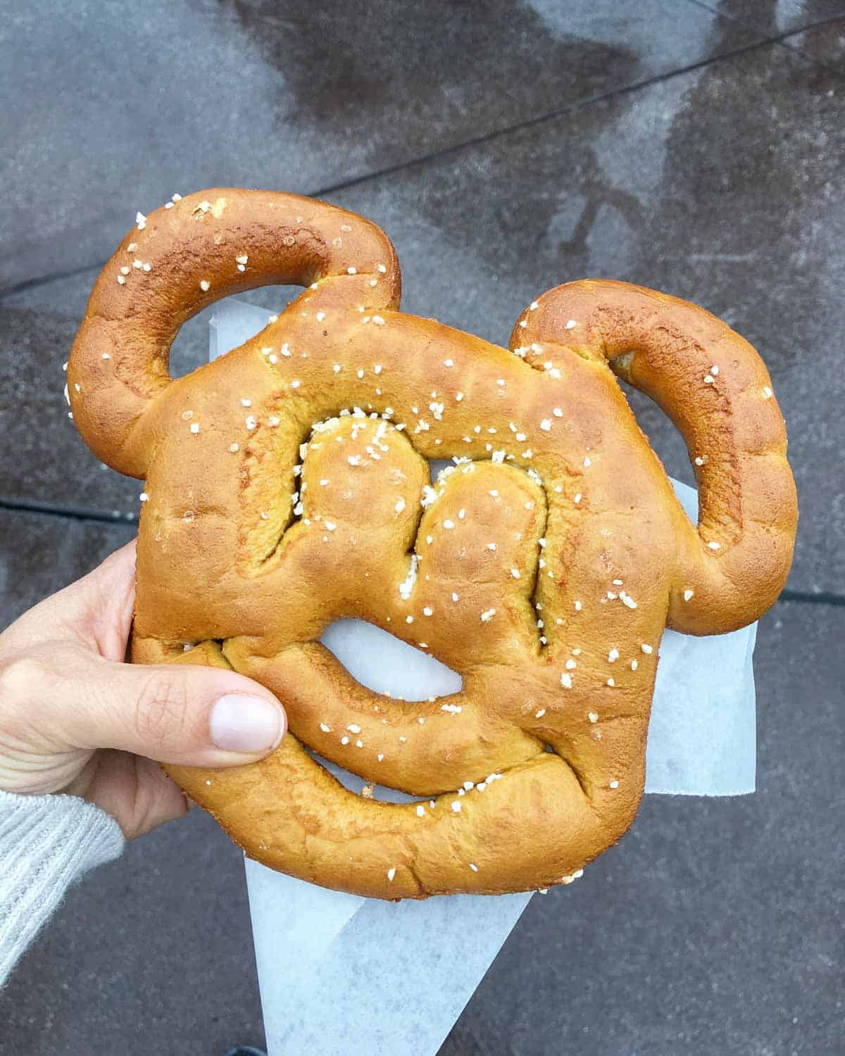 Hand holding a mickey mouse shaped soft pretzel sprinkled with salt.
