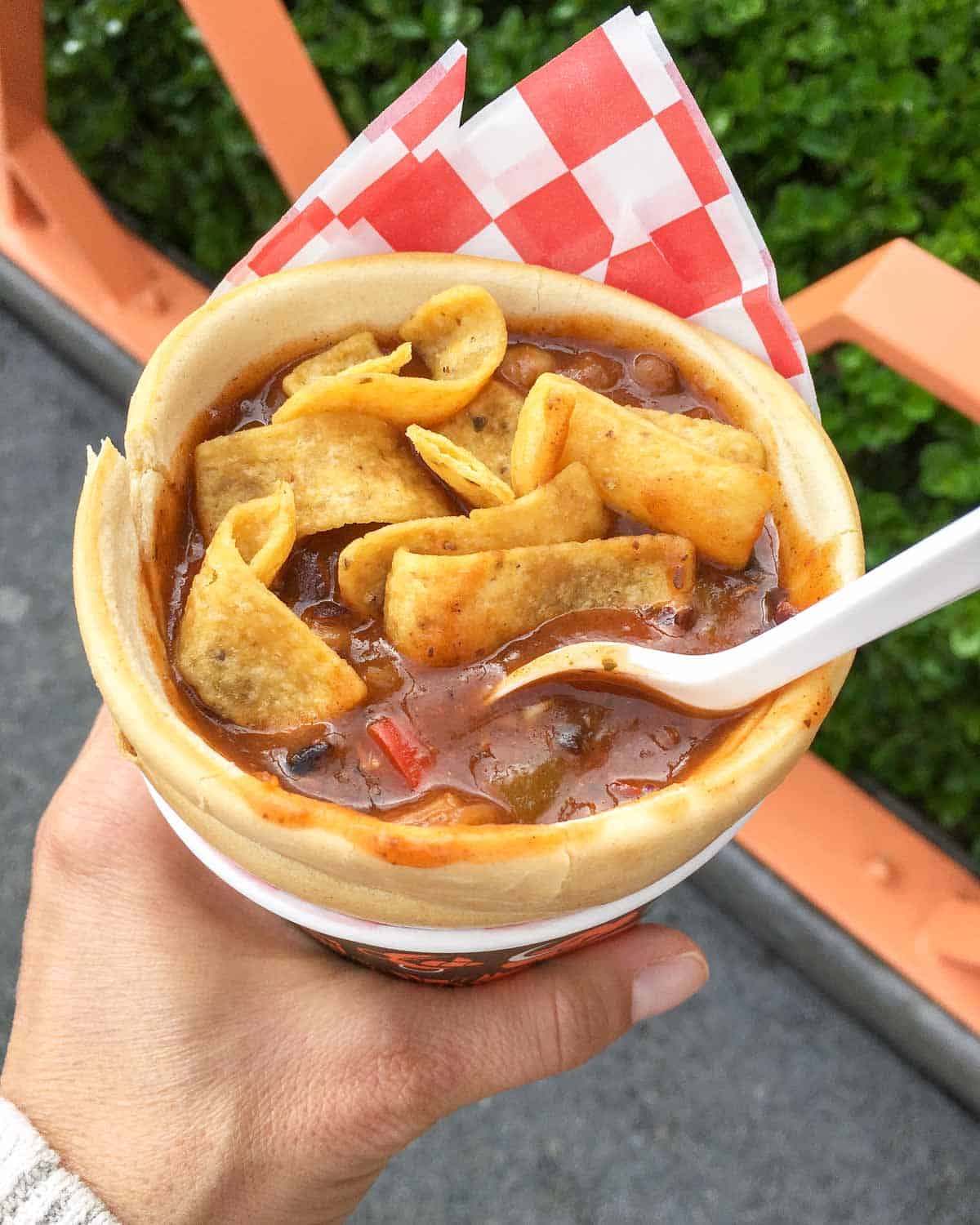 Hand holding a pretzel cone filled with chili and corn chips.