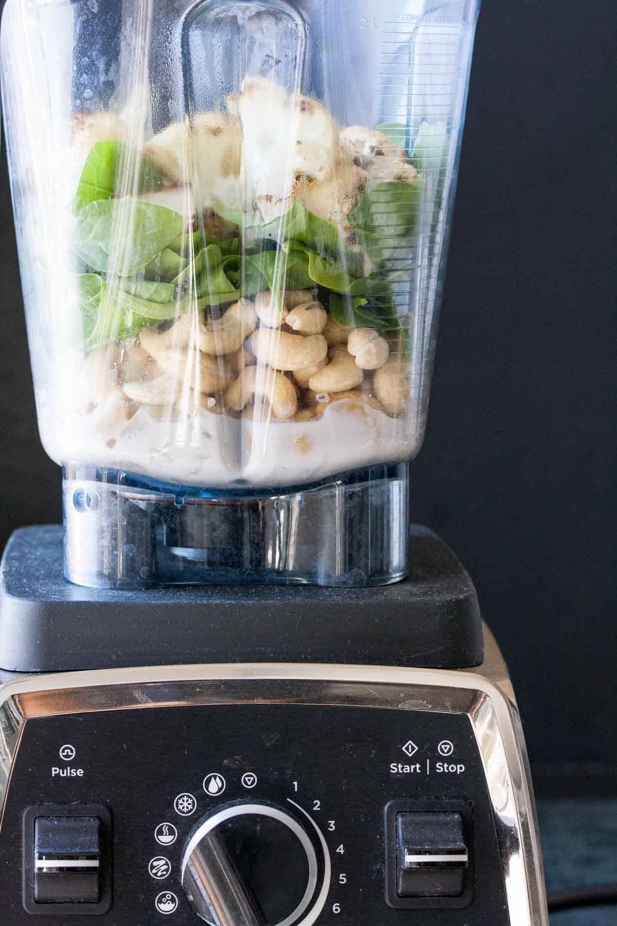 Vitamix blender layered with milk, cashews, spinach and cauliflower.
