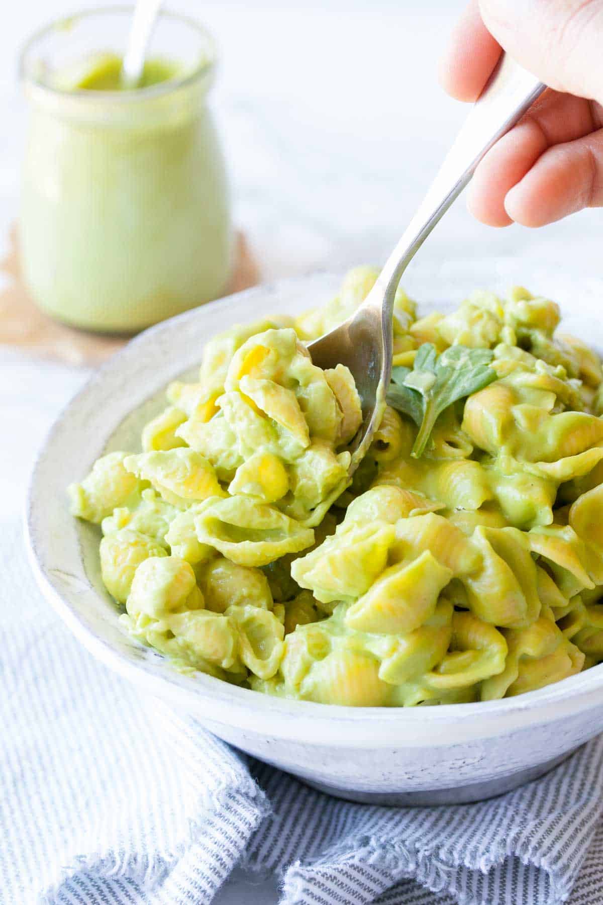 Spoon getting bite out of a white bowl with green mac and cheese.