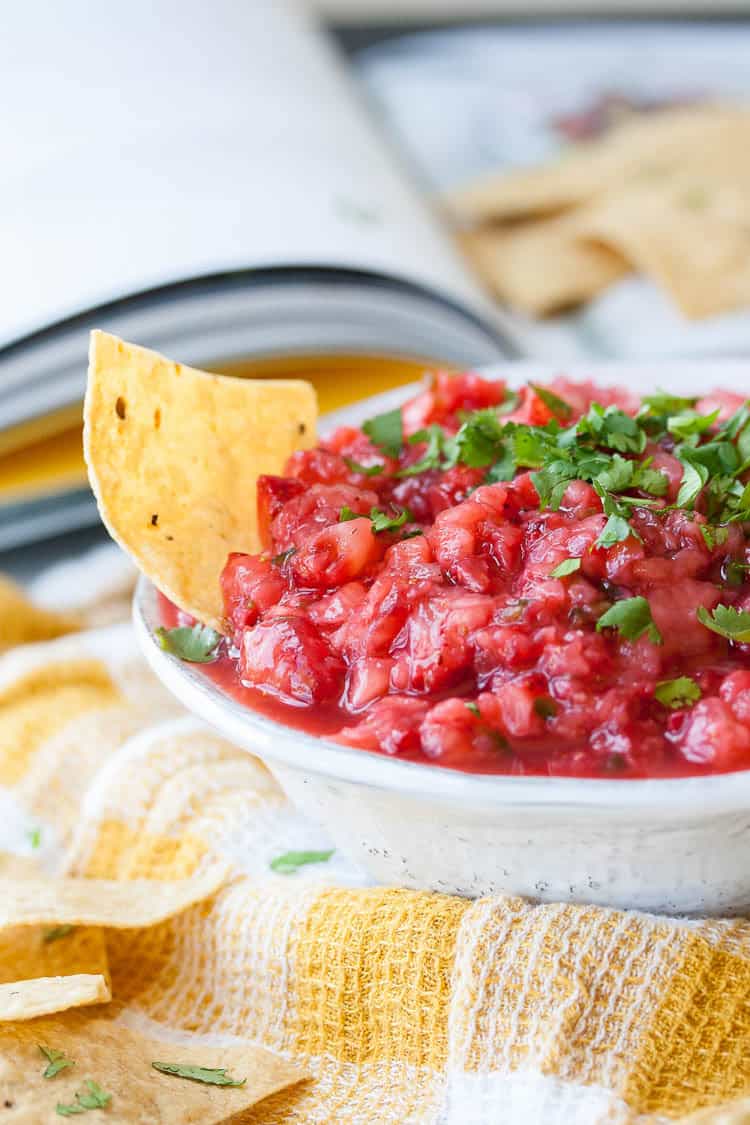 Salsa made from strawberries, chile, minced onion, lime and salt in a small bowl with chips at the side