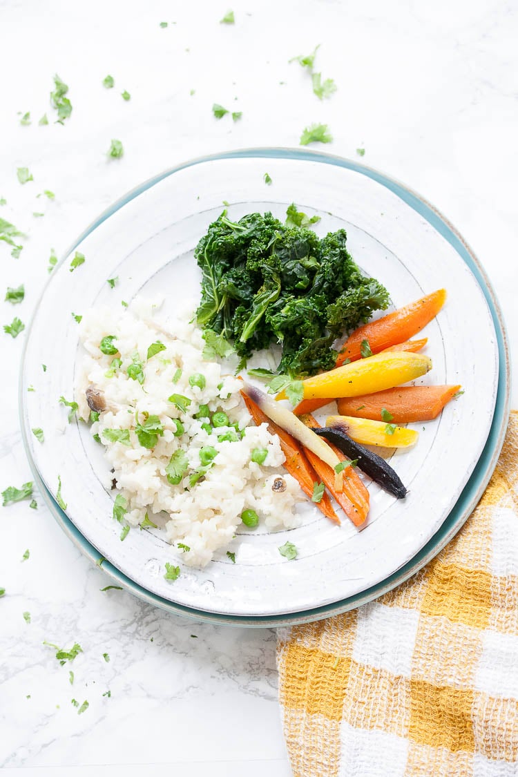 sautéed spinach and kale mix with mushroom risotto and carrots on a white plate