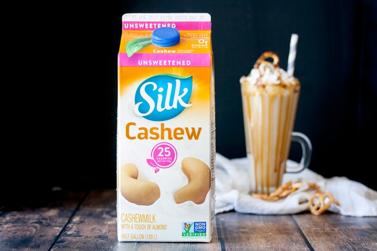 Carton of Silk cashew milk on a wooden table with a smoothie in the background
