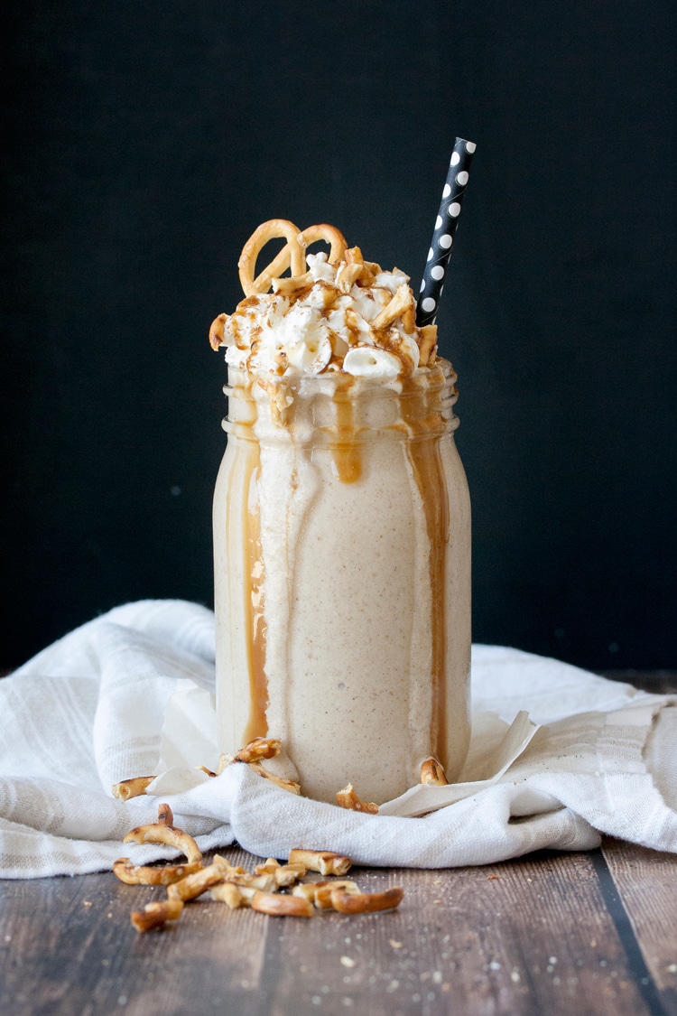Glass jar filled with an oatmeal cookie smoothie with salted caramel and pretzels on top