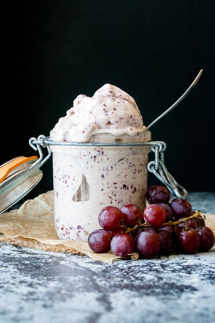 2 ingredient instant frozen yogurt made with frozen red grapes in a glass jar with a spoon and red grapes beside it