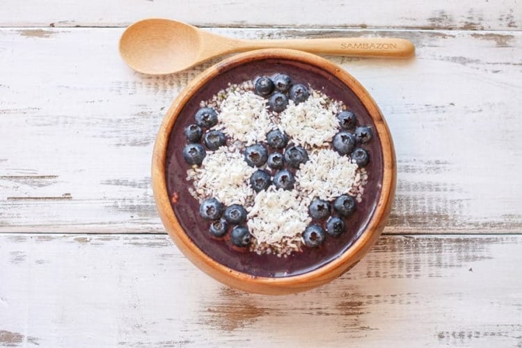 Overhead shot of a Blueberry peach pecan acai smoothie bowl and wooden spoon