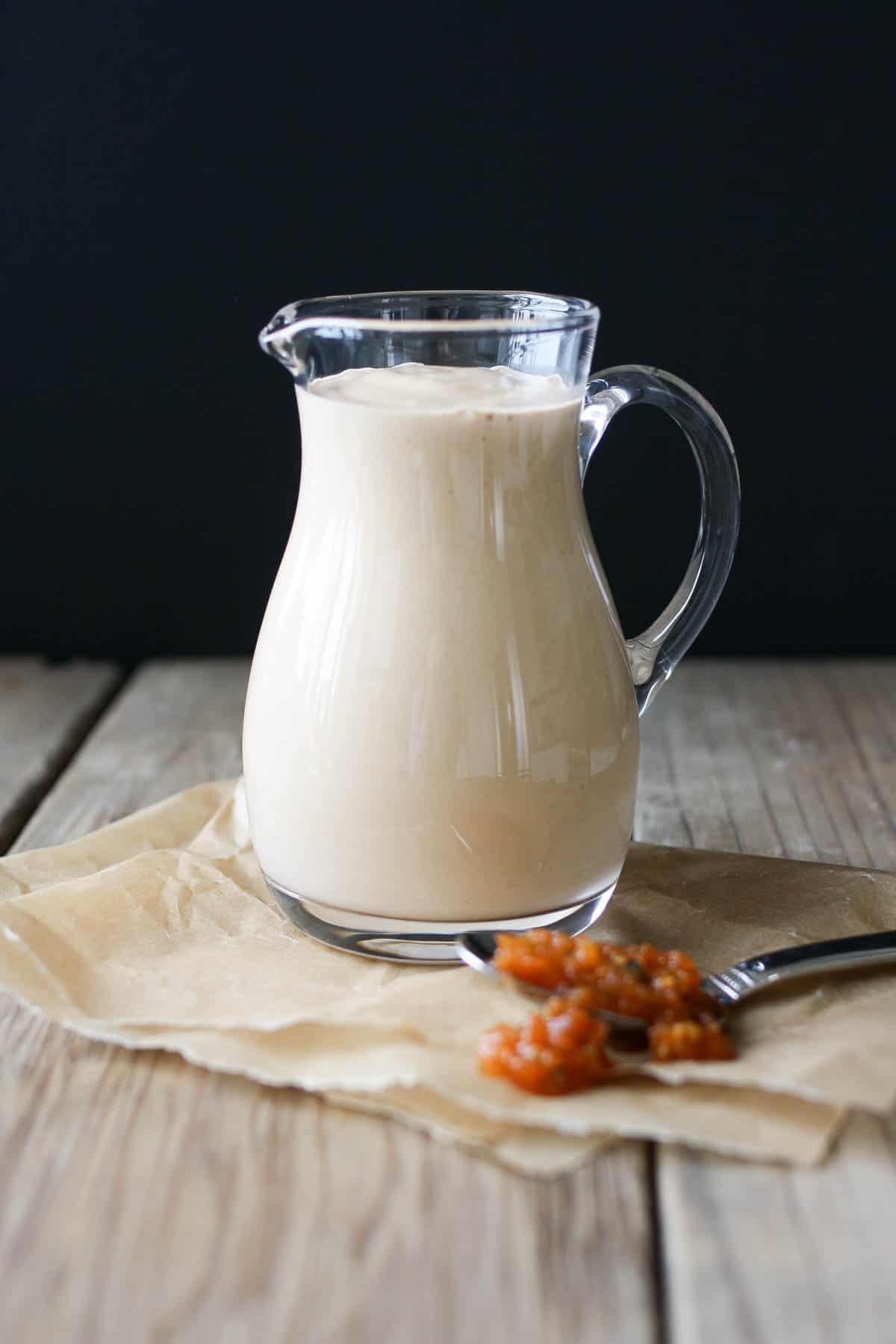 A glass jug filled with crema on a wooden surface