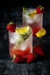 A strawberry vodka cocktail in two textured glasses with lemon, strawberry and thyme garnishes.