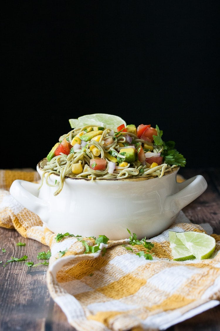 A Mexican pasta salad i n a white bowl topped with veggies and lime