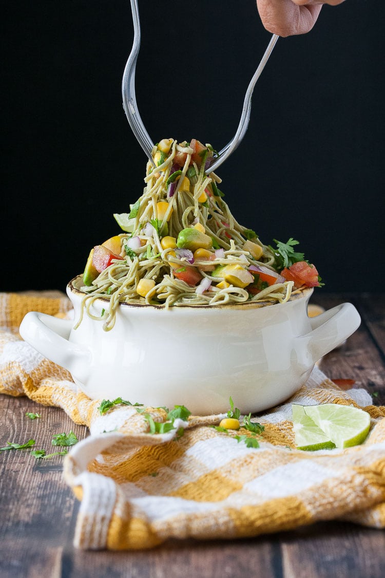 A close up of two forks picking up some mexican pasta salad from a white bowl