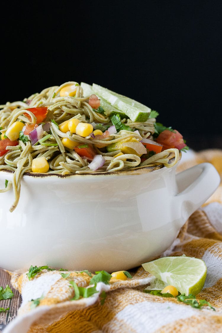 A side shot a mexican pasta salad in a white bowl topped with lime wedges