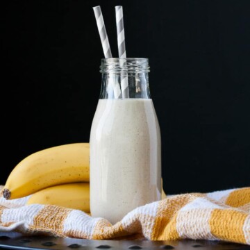 Vegan banana milk in a glass milk bottle with two straws