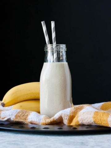 Vegan banana milk in a glass milk bottle with two straws