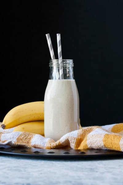 Vegan banana milk in a glass milk bottle with two straws