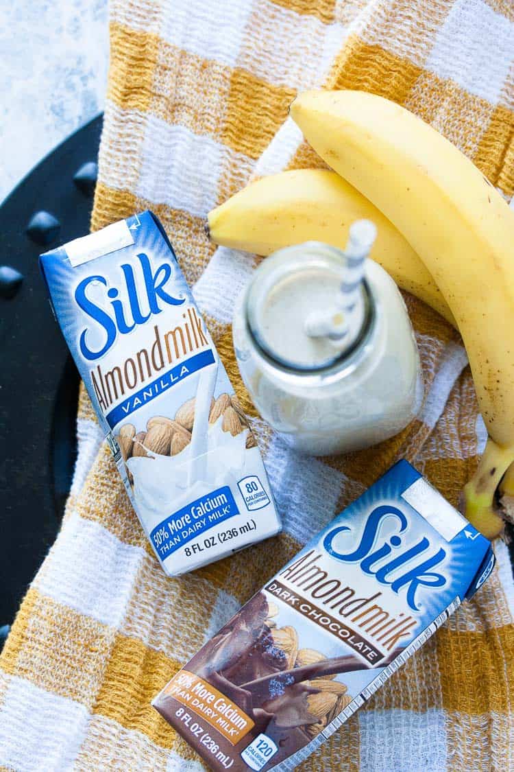 Silk single serving almond milk in small cartons laying on a dish towel with bananas at the side