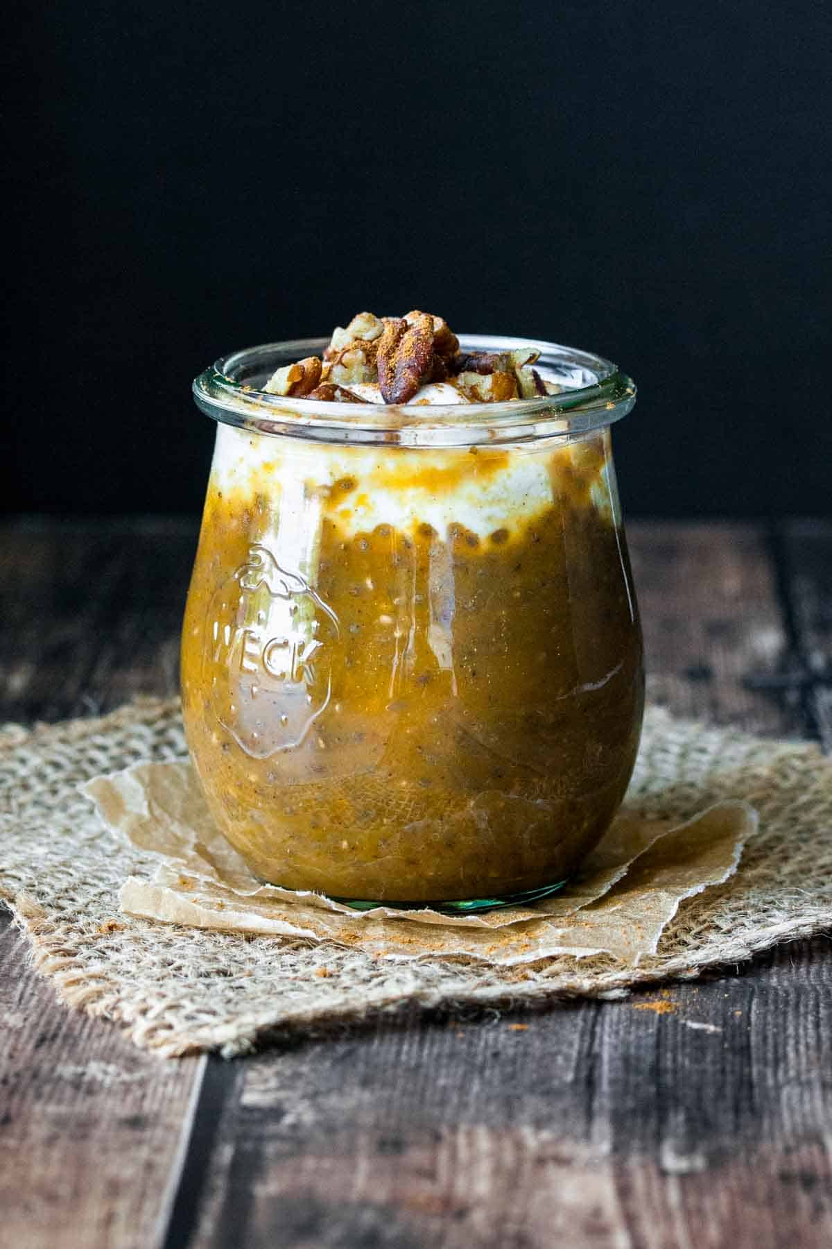 A glass jar with pumpkin chia pudding topped with a cream and nuts.