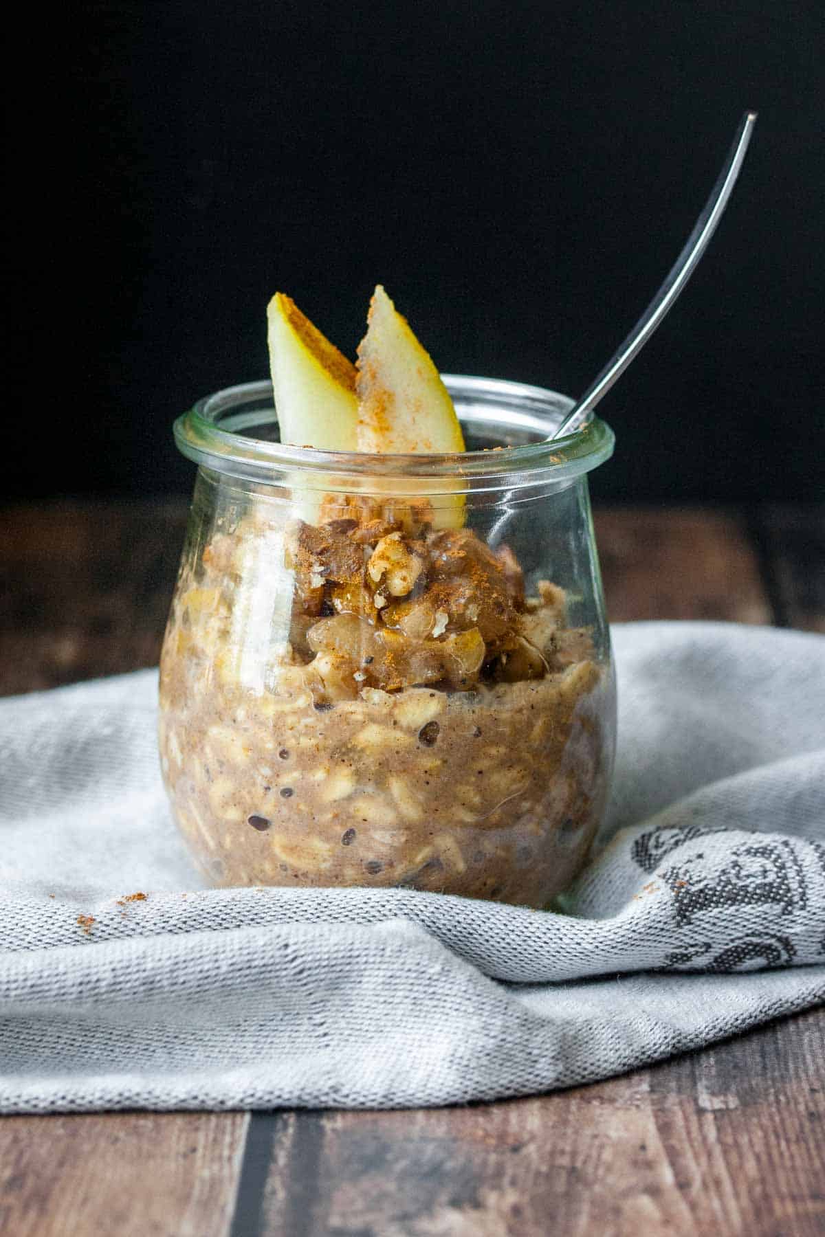 Chai spiced pear overnight oats in a glass jar topped with slices of pear sitting on a blue dishcloth 