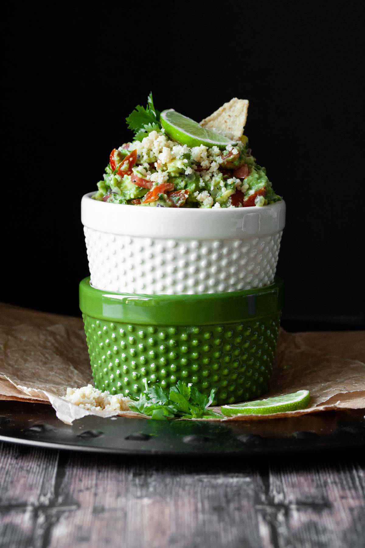 Two bowls stacked on top of each other and top one filled with fully loaded guacamole with vegan cotija cheese