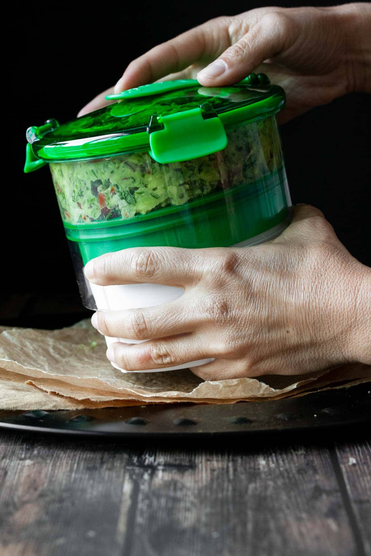 Two hands closing a storage container filled with a loaded guacamole.